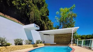 Piscina retangular com superfície de água azul translúcida, rodeada por piso de pedras e borda de tijolos vermelhos.