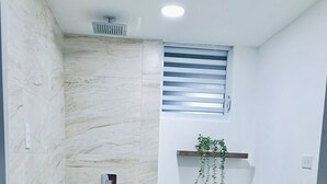 Casa de banho com chuveiro, sanita e uma pequena janela.