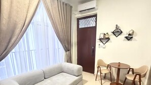 Una sala de estar con un sofá, una mesa de centro con un jarrón, una mesa de comedor con sillas y un adorno en la pared.
