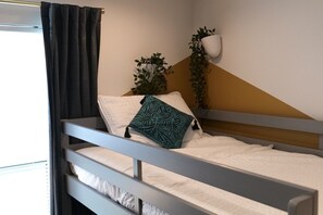 Ein Einzelbett mit weißer Bettwäsche, einem grauen Kopfteil und einem dunkelgrünen, halb geöffneten Vorhang.