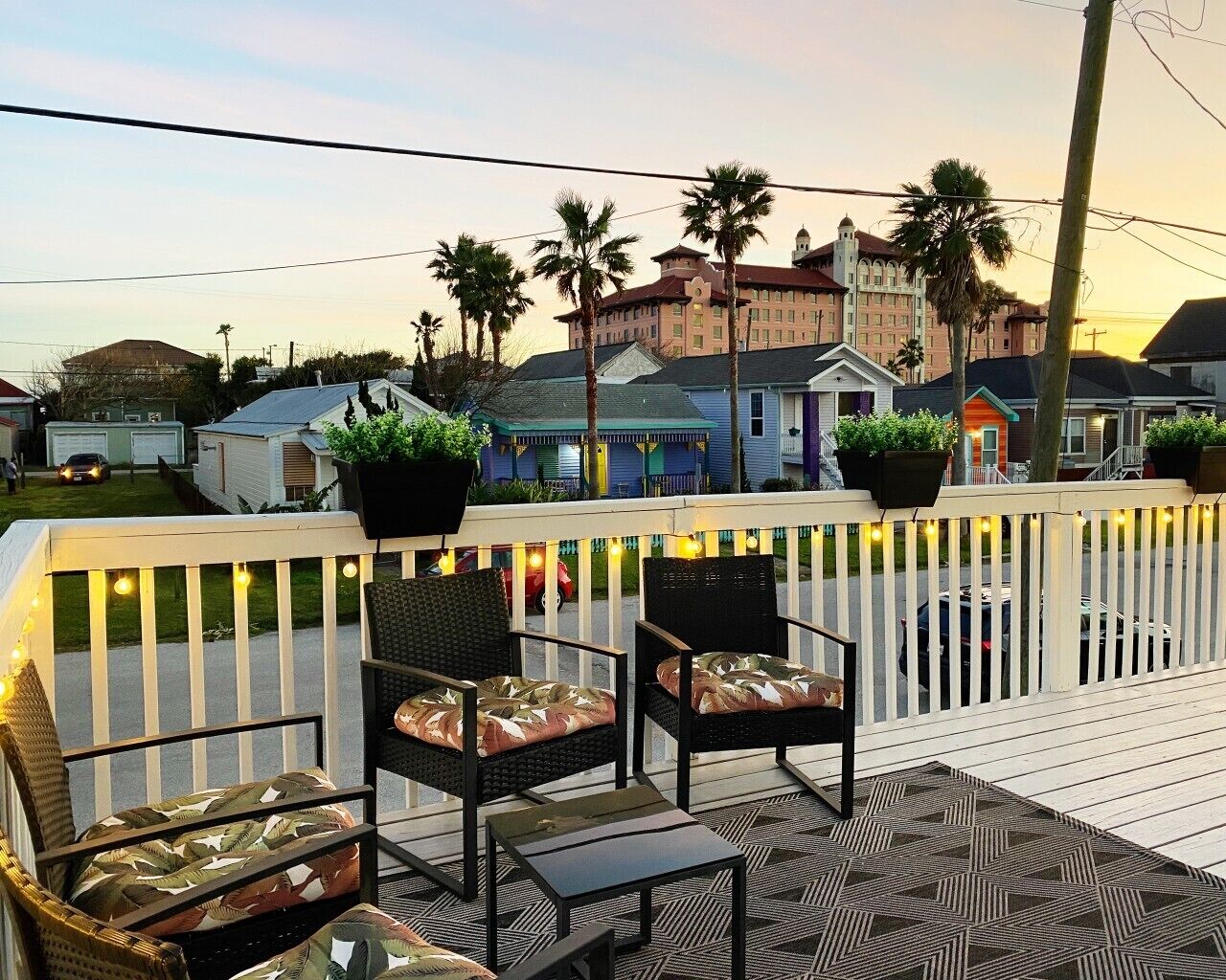 Une terrasse dotée de mobilier d’extérieur, une clôture blanche en bois et une vue sur les bâtiments qui se dressent à l’arrière-plan.