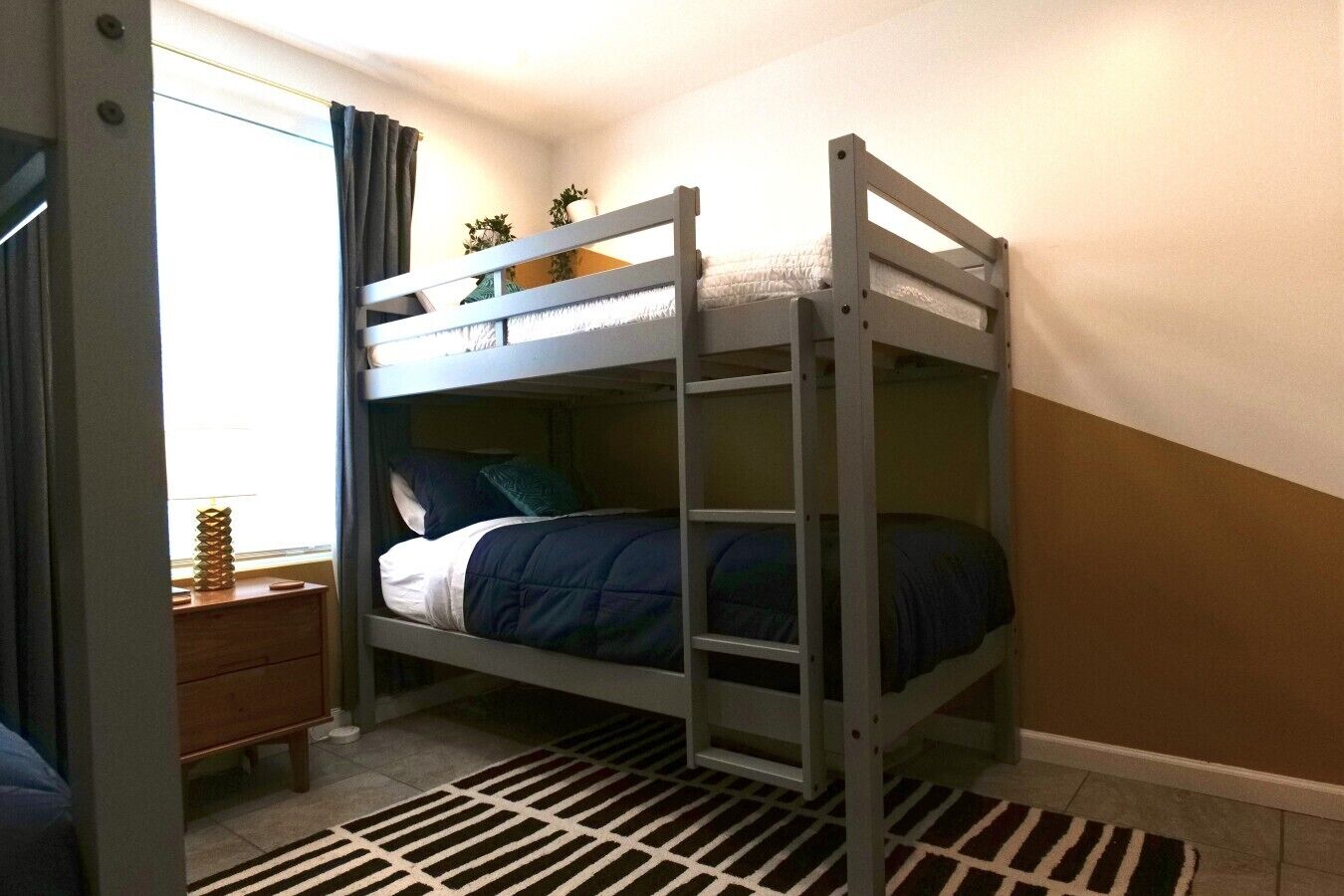 Un lit superposé avec une échelle, une table de chevet avec une lampe et un tapis à motifs.