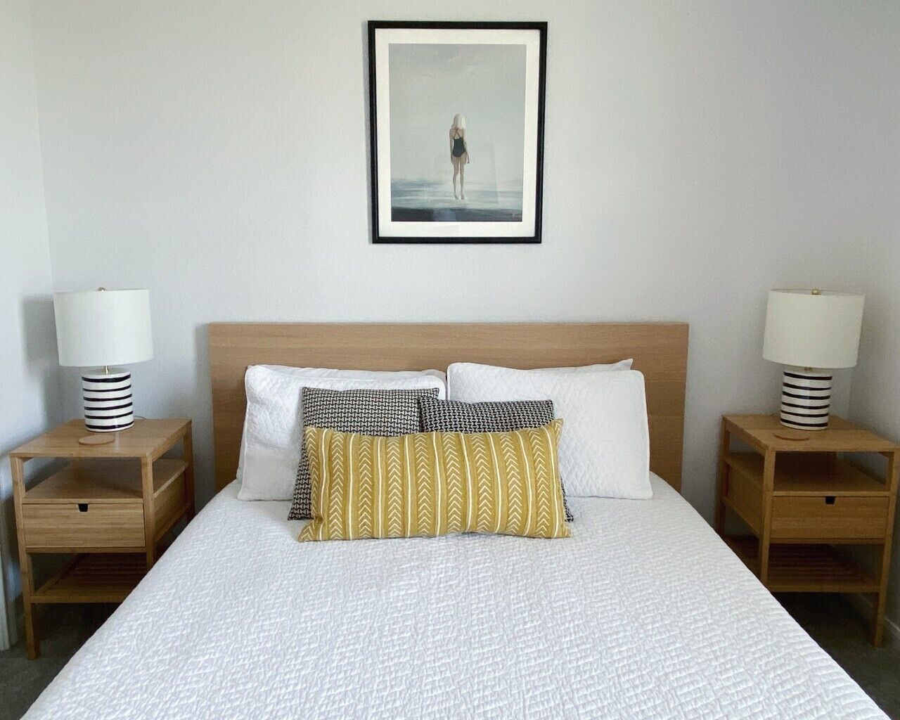 A hotel room with a large bed, two bedside tables, a framed picture on the wall, and a lamp on each table.