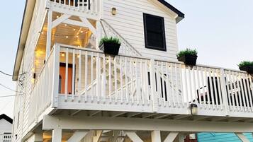 A two-story building with a balcony, outdoor lighting, and potted plants.