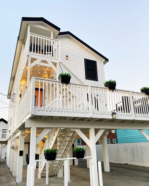 A two-story building with a balcony, outdoor lighting, and potted plants. - Soleil House - Unit A- Close to beach/downtown (Galveston)