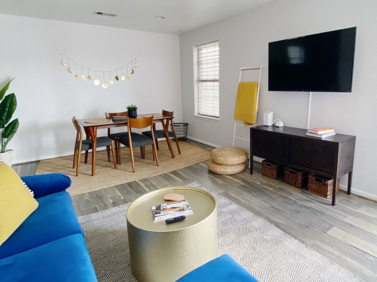 A living room with a sofa, coffee table, TV, and a dining area with chairs and a table.