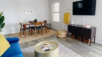 A living room with a sofa, coffee table, TV, and a dining area with chairs and a table.