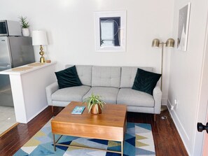 Ein Wohnzimmer mit einer Couch, einem Couchtisch und einer kleinen Küchenzeile mit einer Mikrowelle.