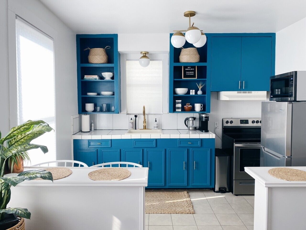 Una cocina moderna con armarios azules, encimeras blancas, un refrigerador de acero inoxidable y un horno integrado.