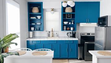 Una cocina moderna con armarios azules, encimeras blancas, un refrigerador de acero inoxidable y un horno integrado.