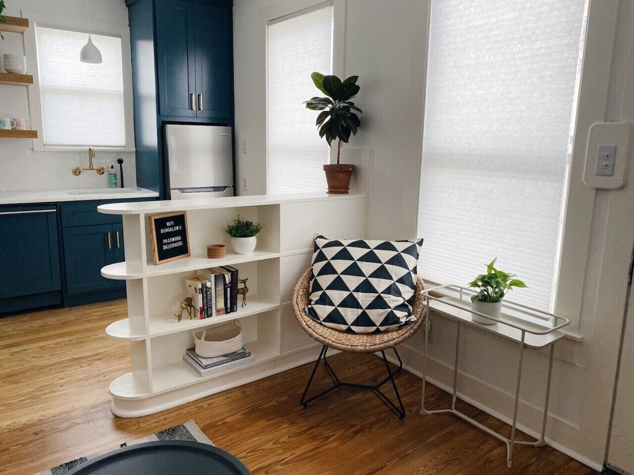 Una cocina moderna con gabinetes azul oscuro, encimera blanca y una silla de mimbre con un cojín geométrico.