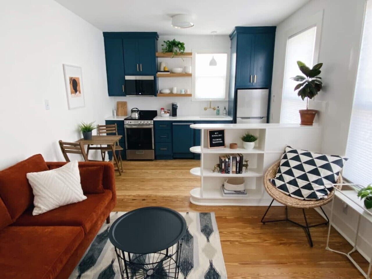 A modern kitchen with dark blue cabinets, a dining area with a red sofa, and a black and white patterned rug.