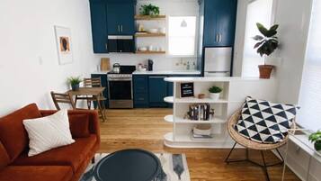 A modern kitchen with dark blue cabinets, a dining area with a red sofa, and a black and white patterned rug.