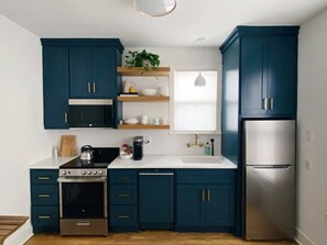 Een kleine keuken met donkerblauwe kastjes, een roestvrijstalen koelkast, een magnetron, een fornuis en een spoelbak.