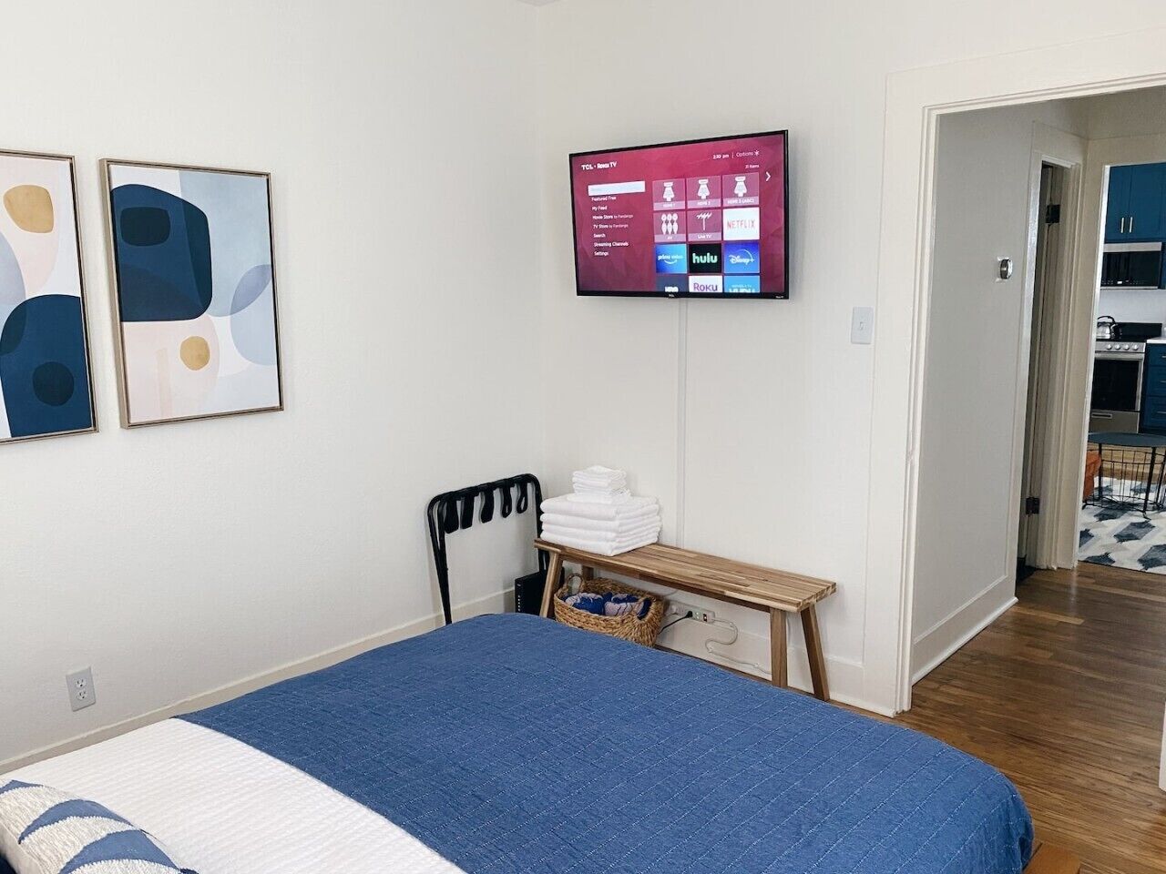 A bedroom with a bed, a TV mounted on the wall, a desk with a chair, and a door leading to a bathroom.