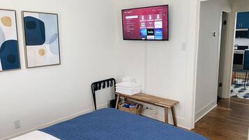 A bedroom with a bed, a TV mounted on the wall, a desk with a chair, and a door leading to a bathroom.