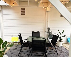 Een terras met een ronde tafel en stoelen, sfeerverlichting, een bloempot en een trap.