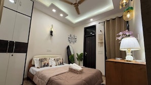Quarto com cama, guarda-roupa, ventoinha no teto, quadro na parede e abajur.
