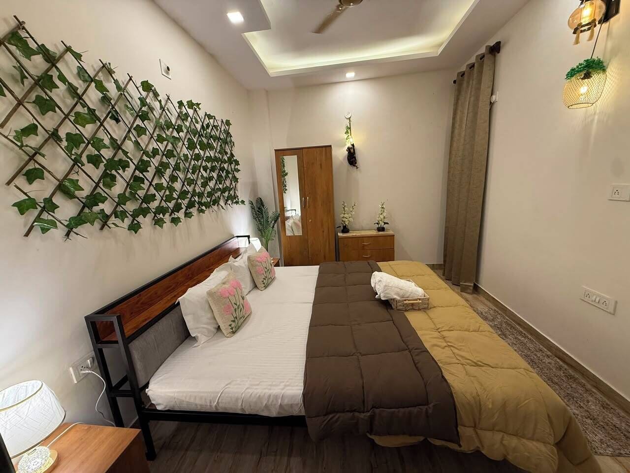 A bedroom with a bed, bedside table, wall-mounted plants, a mirror, and a ceiling fan.