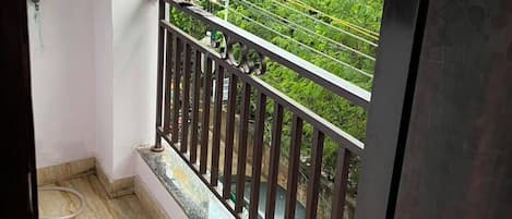Un balcon doté d’une balustrade en métal, un tissu vert suspendu au mur et une vue sur une végétation luxuriante.
