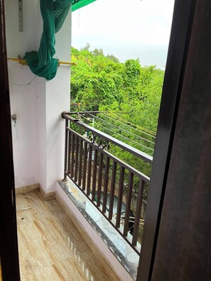 Ein Balkon mit Metallgeländer, ein grüner Stoff, der an der Wand hängt, und Blick auf üppiges Grün.