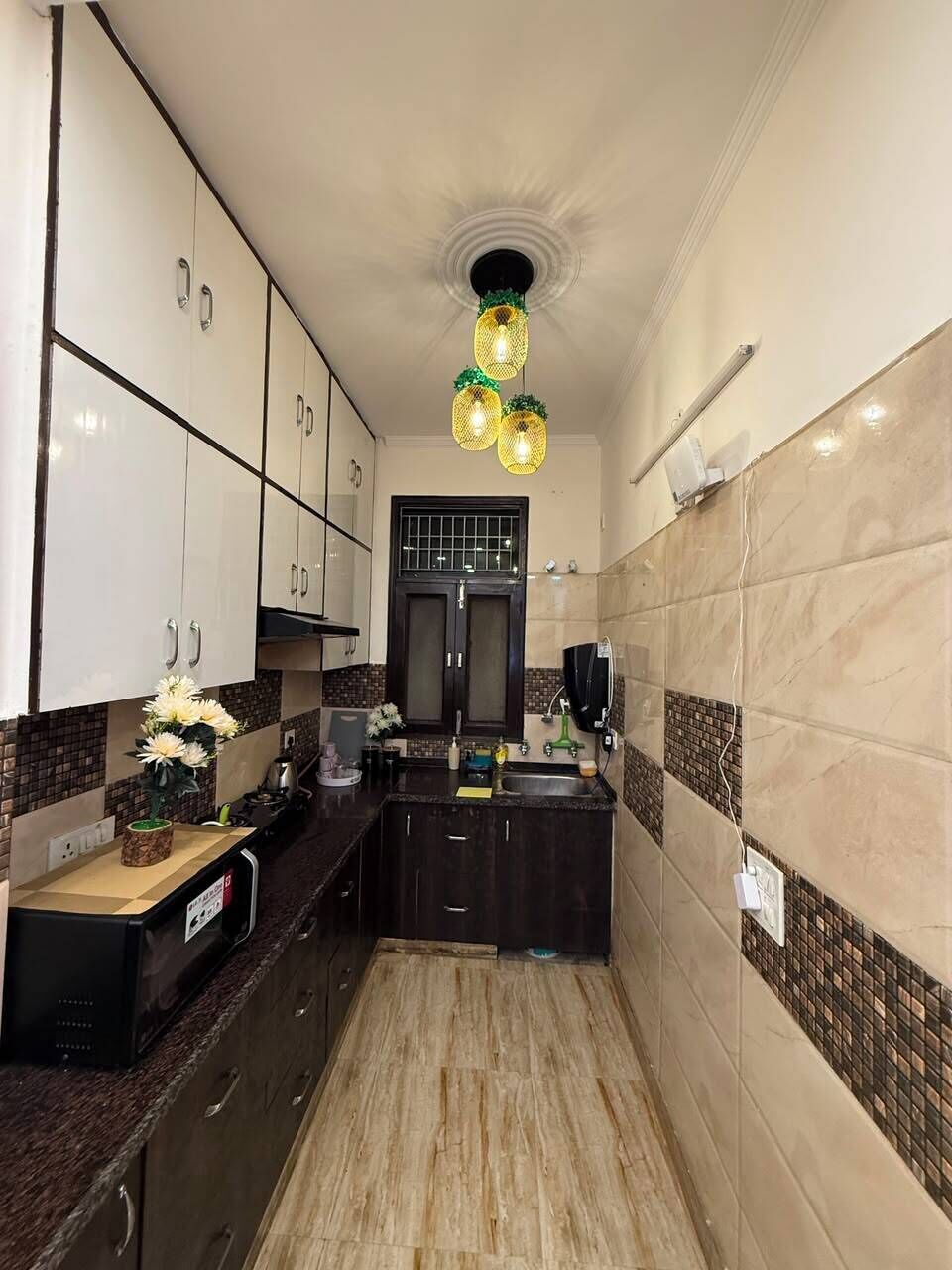 A narrow kitchen with dark cabinets, a black countertop, and a tiled backsplash.