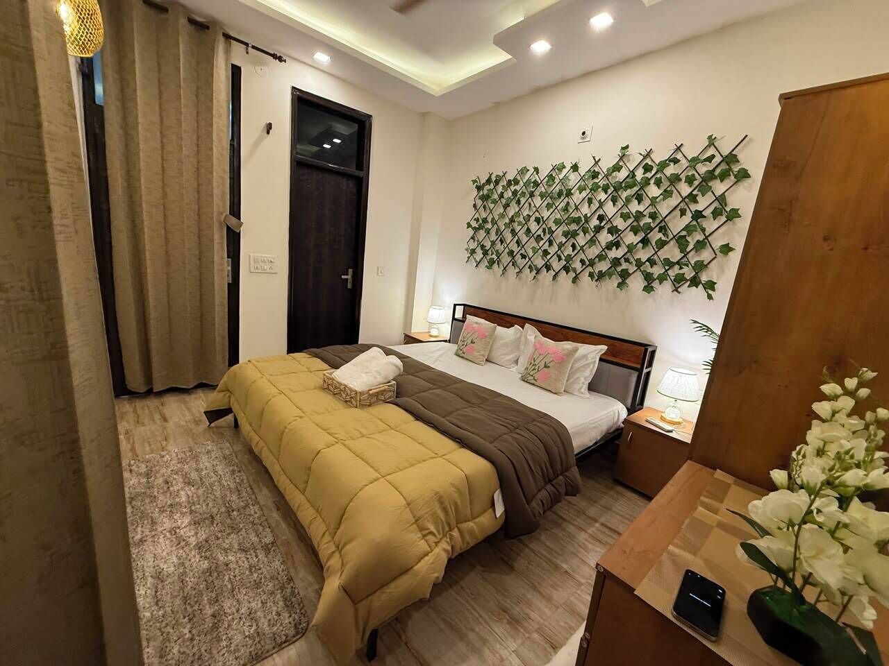 Een hotelkamer met een bed, nachtkastje, lamp en een plantdecoratie aan de muur.