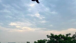 Avião voando sob céu claro, com árvores ao fundo.