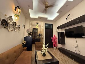 A modern living room with a sofa, dining table, and a flat-screen TV mounted on the wall.