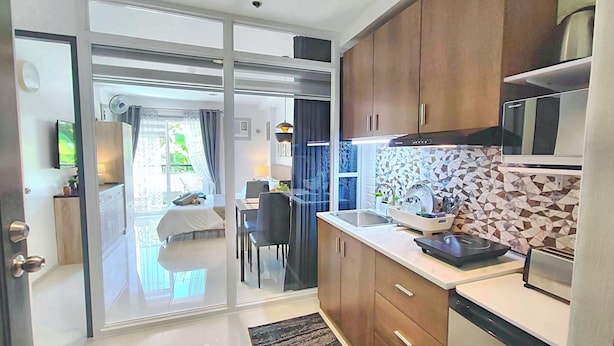 A modern kitchen with a microwave, toaster, and sink. There is a dining area with a table and chairs. The kitchen has a tiled backsplash and wooden cabinets. - Cozy CityCondo near CPU, with a balcony and park view, 2 floors, fiber-optic Wi-Fi, free parking (Iloilo City)