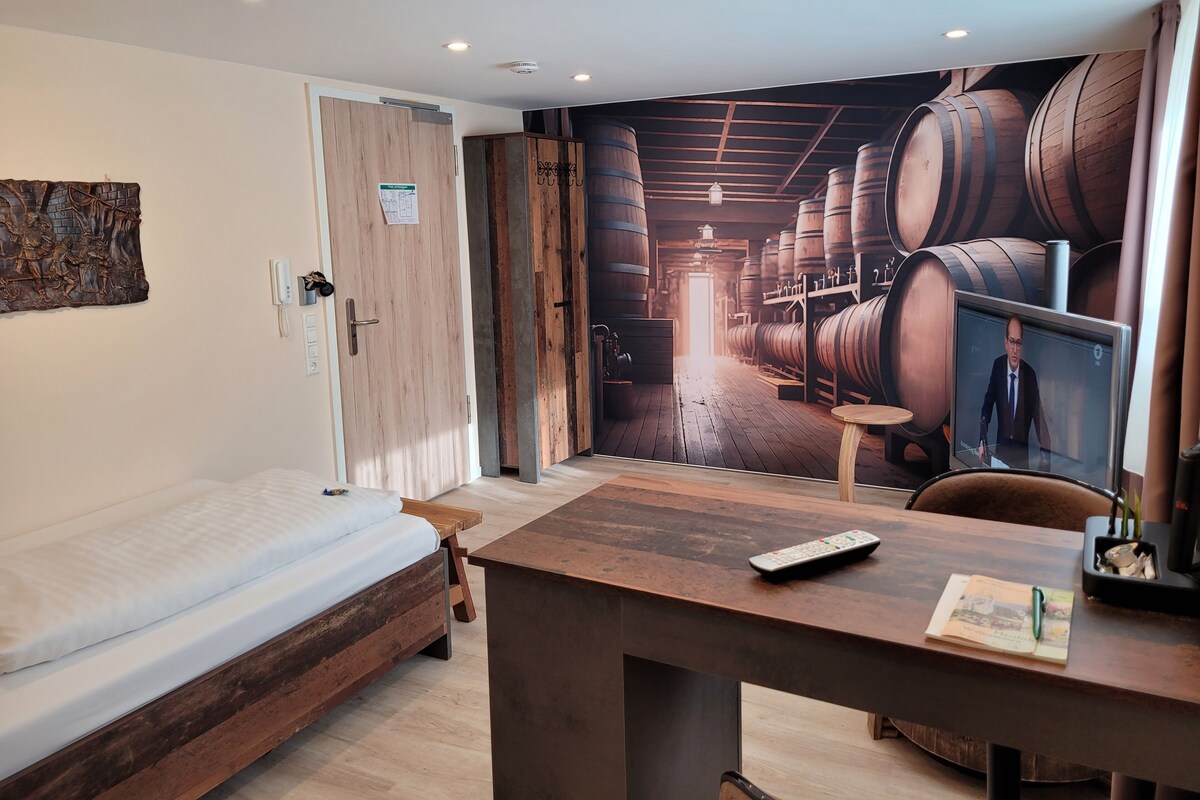 Una habitación con cama, escritorio con control remoto y un mural de barriles de vino.