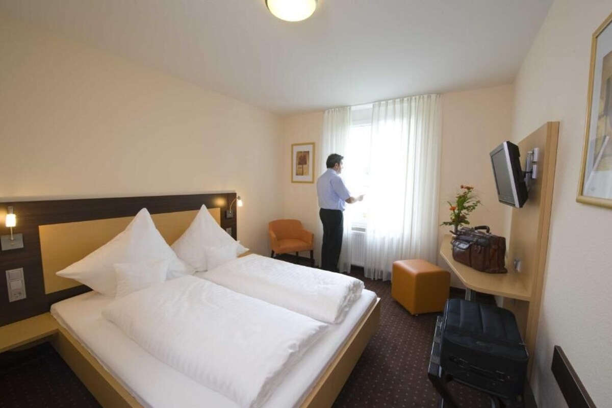 Habitación de hotel con cama doble, escritorio con silla, televisión y ventana con cortinas.