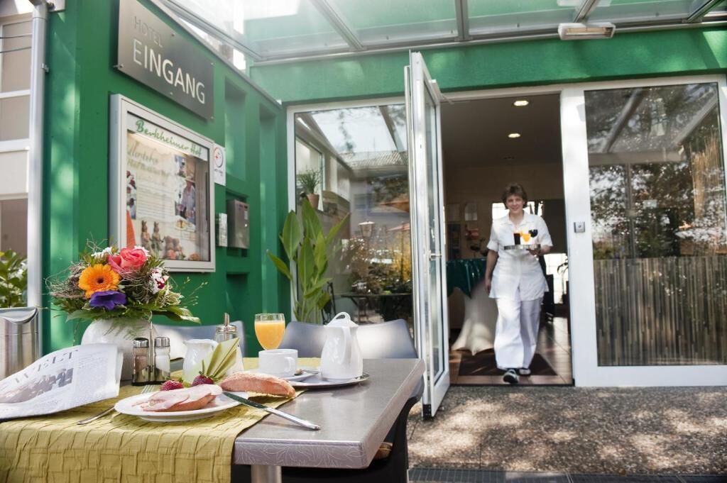 A hotel entrance with a green exterior, a table set with breakfast, and a person in uniform.