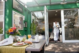 Ein Hotel mit grüner Fassade, ein Tisch gedeckt für das Frühstück und eine Person in Uniform.