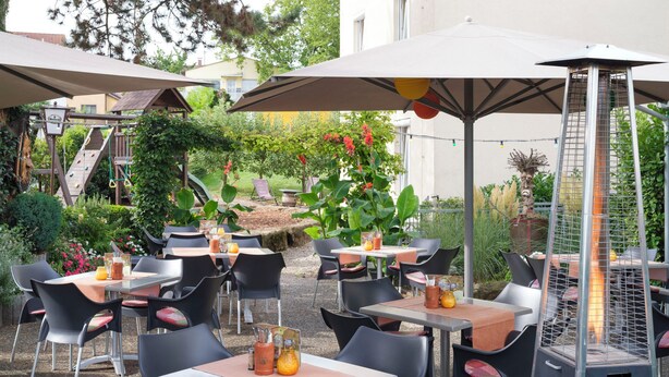 An outdoor patio area with tables and chairs, some with umbrellas, surrounded by greenery and a climbing structure. - Hotel Berkheimer Hof (Esslingen am Neckar)