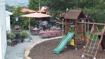 Un espace de jeux pour enfants avec un toboggan, entouré de sièges et de tables en plein air.