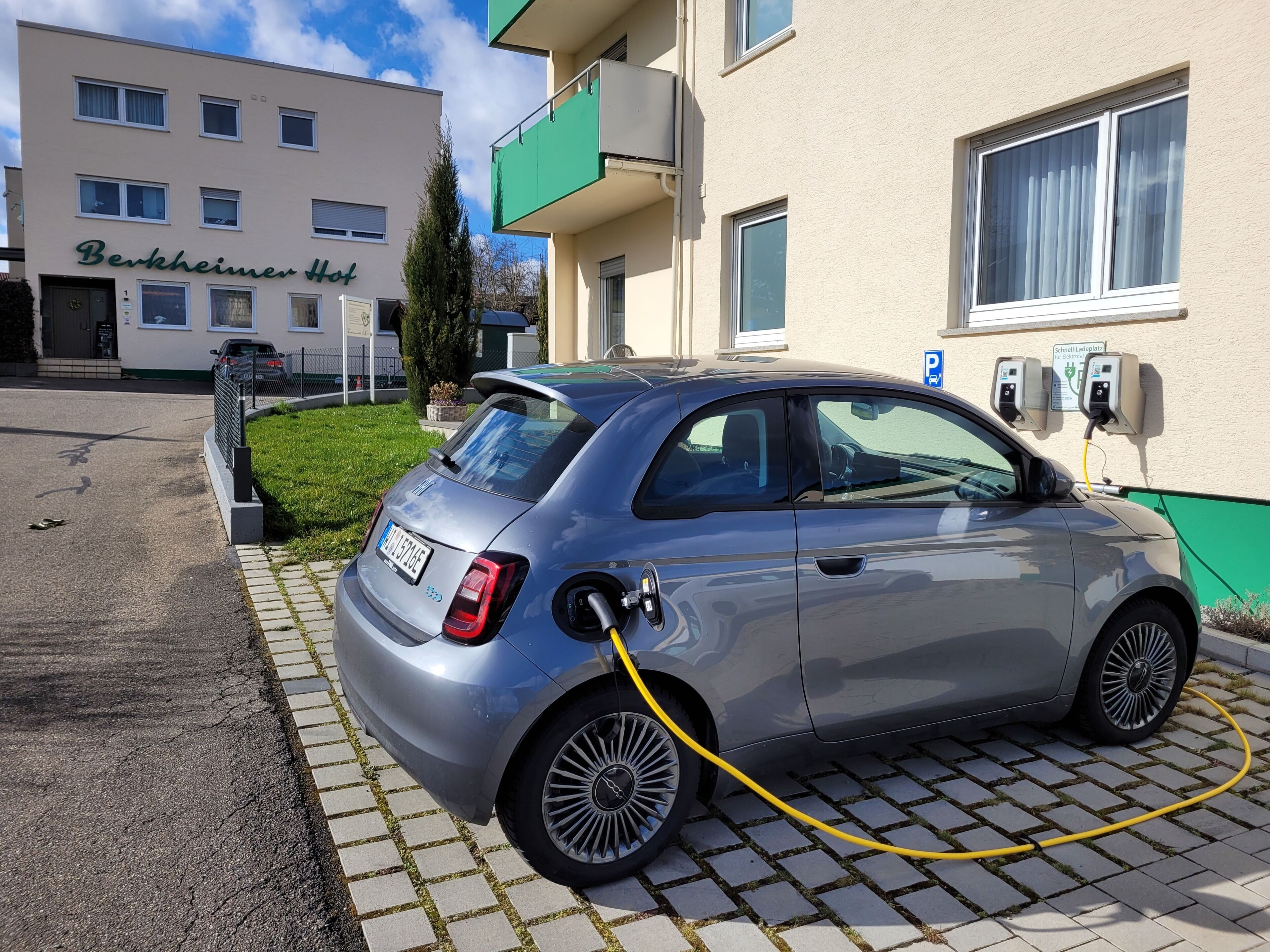 A silver car parked in a driveway with a charging station.