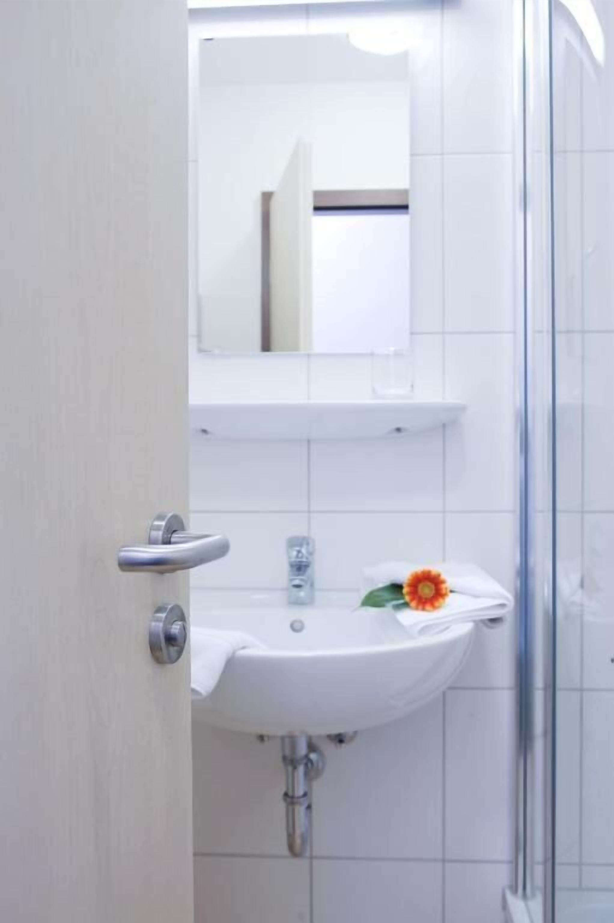 Un baño con lavamanos blanco, espejo y zona de ducha.
