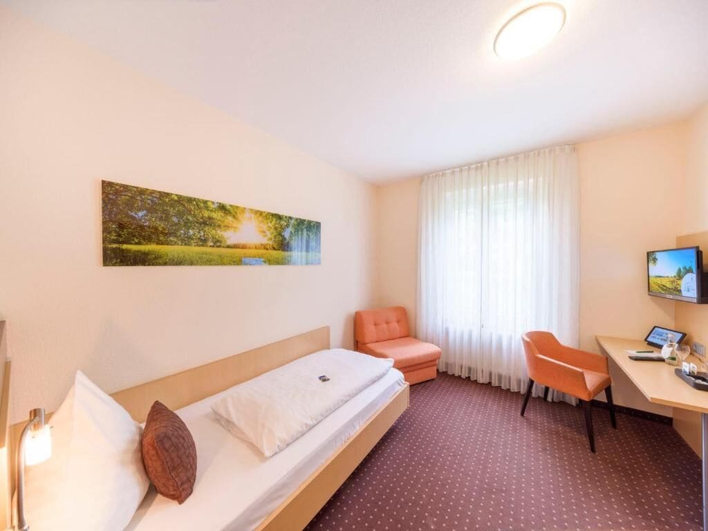 A hotel room with a bed, a desk, a chair, a TV, and a painting on the wall.