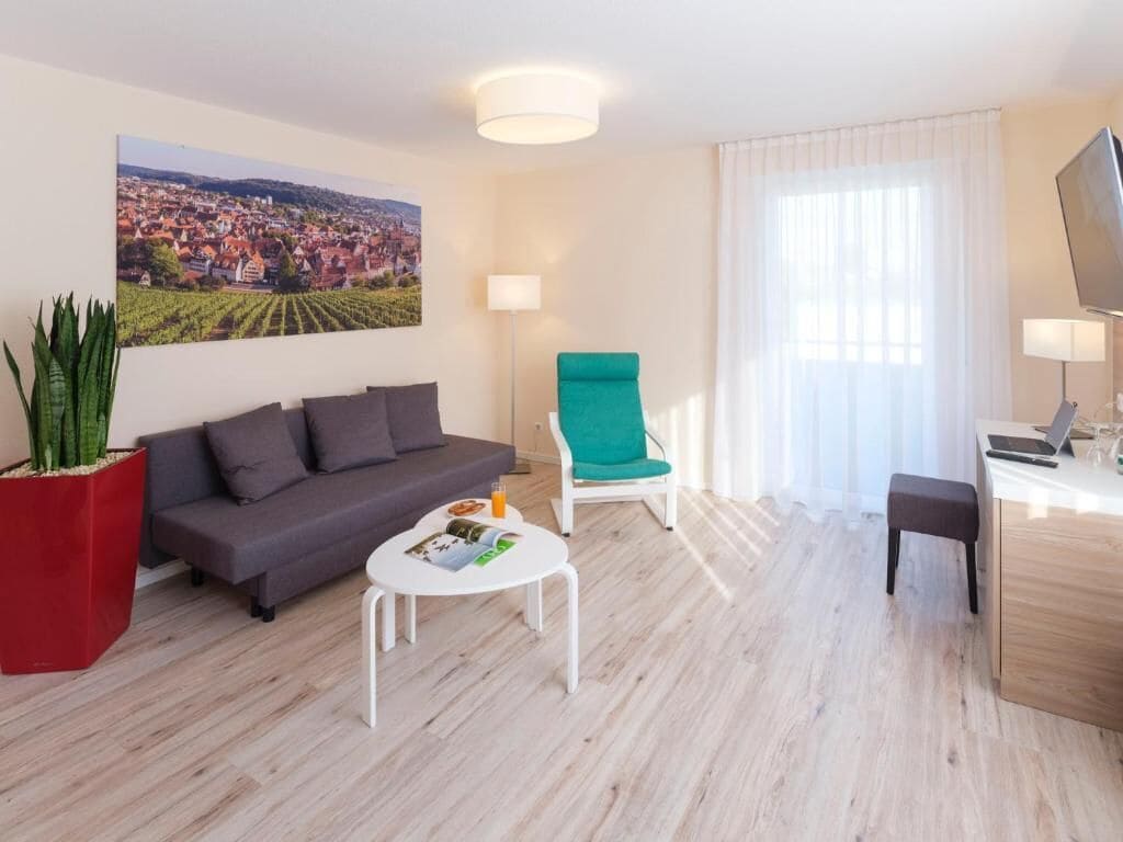 Un salon moderne avec un canapé, un fauteuil vert, une table basse et un bureau avec un ordinateur portable.