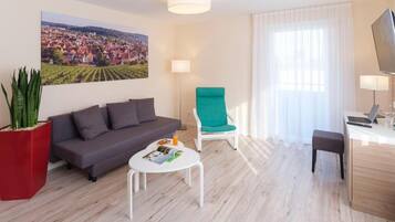 Un salon moderne avec un canapé, un fauteuil vert, une table basse et un bureau avec un ordinateur portable.