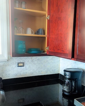 Eine Küche mit Kaffeemaschine, einem Schrank voller Geschirr und einer gefliesten Spritzschutzwand.
