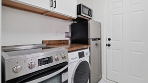 Cozinha equipada com forno embutido, micro-ondas e máquina de lavar roupa, bancada de madeira e porta branca.