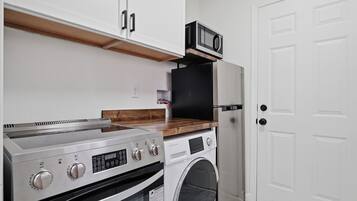 A kitchen with a built-in oven, microwave, and washing machine, a wooden countertop, and a white door.