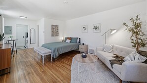 Quarto moderno e bem iluminado com cama, mesa de cabeceira e um sofá.