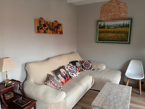 Ein Wohnzimmer mit einer Couch, gemusterten Kissen, einer Lampe, einem kleinen Tisch, einer Wanddekoration und einem gerahmten Gemälde.