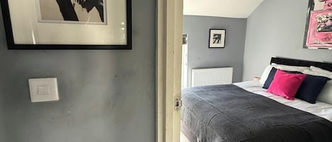 A bedroom with a bed, a framed abstract painting, a radiator, and a door leading to another room.