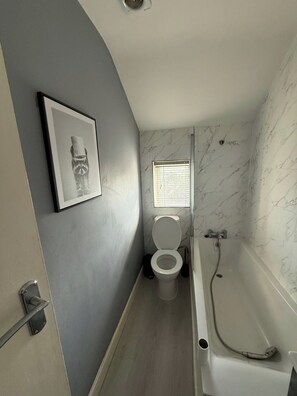 Ein Badezimmer mit Toilette, einem gerahmten Bild an der Wand und einer Badewanne.