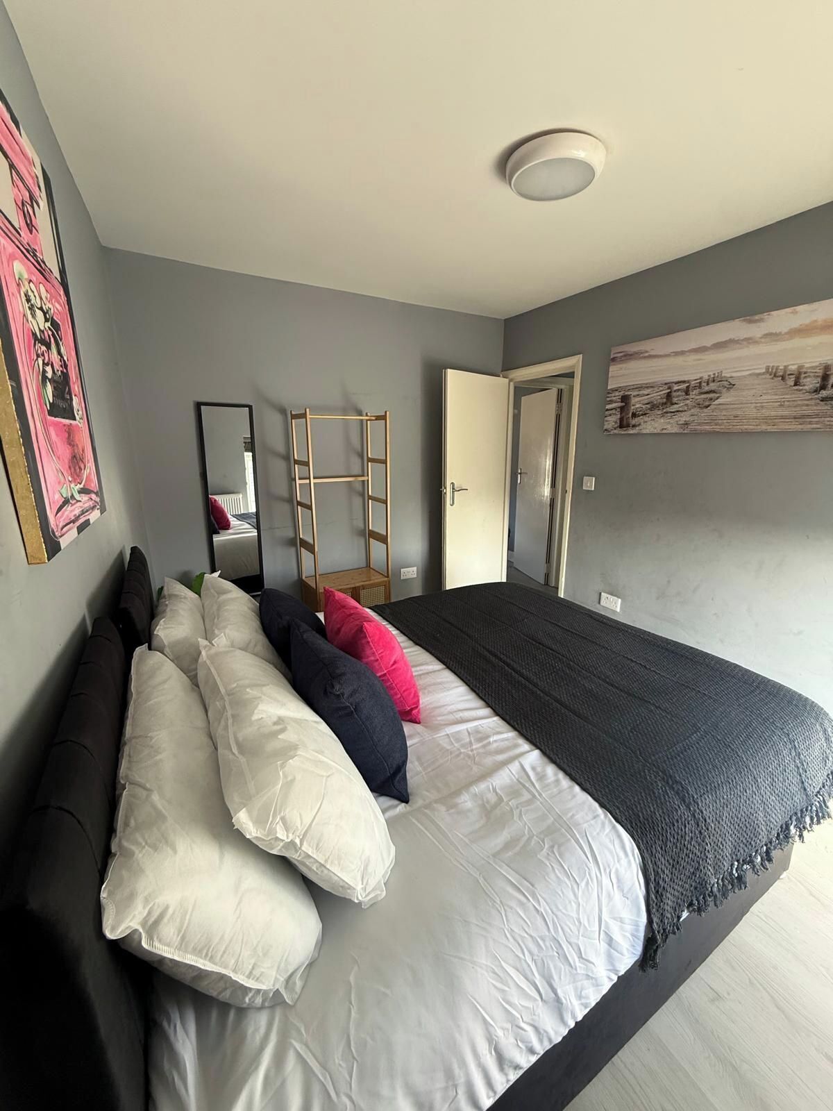Una camera da letto con un letto, cuscini, una scala, una porta e un quadro appeso al muro.