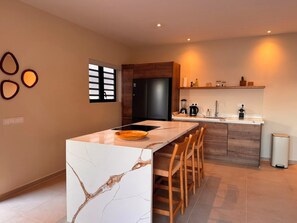 Eine moderne Küche mit einer Marmorinsel, Holzstühlen und einem schwarzen Kühlschrank.